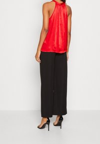 Haut en satin rouge à dos noué, associé à un pantalon large noir et des sandales à talons hauts noires.