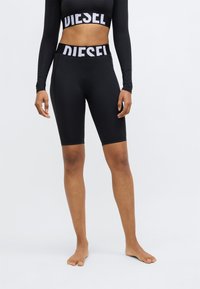 Czarne szorty fitness z szerokim pasem z napisem "DIESEL" w białym kolorze. Gładka faktura, długość do kolan, odpowiednie do aktywności fizycznej.
