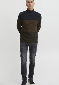 Maglione a collo alto lavorato a maglia con design a blocchi di colore blu navy, marrone e verde oliva. Texture chunky, colletto a costine e vestibilità rilassata.