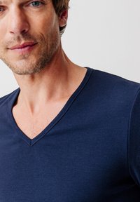T-shirt blu navy con scollo a V realizzato in tessuto morbido. Le maniche corte e il design aderente mettono in risalto la scollatura e le spalle.