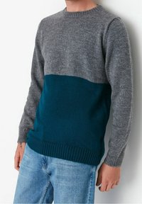 Trui in grijs en teal. De bovenkant is grijs, en de onderkant is teal. Heeft een ronde hals, ribbelzoom en een gestructureerd breipatroon.