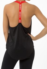 Musta urheilu-toppi, jossa on urheiluselkämuotoilu, takana punainen "JUST DO IT" -olkaimellinen nauha ja kaareva helma. Pehmeää, kevyttä kangasta.