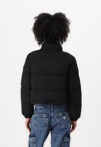 Zwarte pufferjack met een hoge kraag en een gestikte ontwerp. Draag met lichtblauwe cargobroek met opgestikte zakken. Textuur zichtbaar.