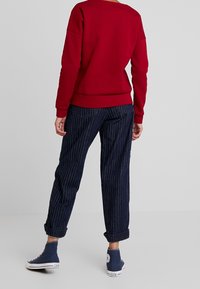 Red sweatshirt with a relaxed fit, paired with dark blue pinstriped trousers. The outfit features rolled cuffs and blue high-top sneakers.
