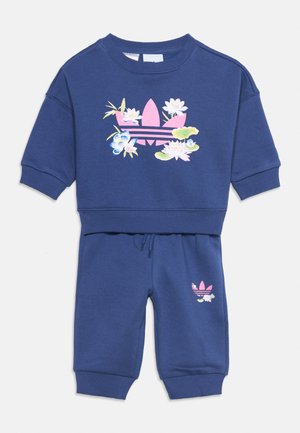 Marineblauw peutersweatshirt- en broekset met roze Adidas trefoil-logo, versierd met witte en blauwe bloemmotieven.