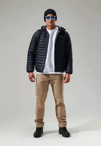 Μαύρο μπουφάν με οριζόντιες ραφές, λευκή μπλούζα, καφέ cargo παντελόνι, μαύρο σκουφί, μπλε γυαλιά ηλίου και μαύρες μπότες.