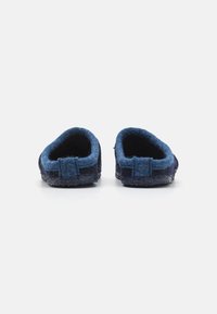 Wool slippers in dark blue with a soft, textured surface, rounded shape, and open back design. Feature minimal stitching accents.