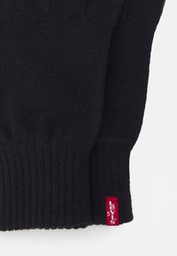 Sort striktrøje med ribbet tekstur og et rødt Levi's mærke ved kanten. Designet inkluderer en tætsiddende mansjet.