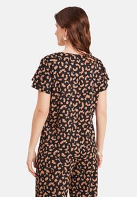 Schwarze Bluse mit einem Leopardenmuster in Hellbraun, kurzen Rüschensäumen und lockerer Passform. Weicher Stoff mit strukturiertem Aussehen.