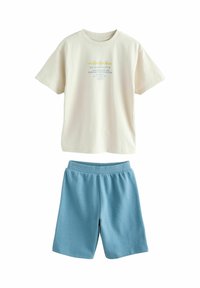 Lys beige bomuld T-shirt med trykt design, kombineret med blå ribstrikkede shorts. Outfittet har en afslappet pasform og elastisk taljebånd.