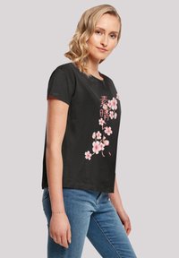 Černé bavlněné tričko s potiskem růžových sakur a japonským textem na přední straně. Krátké rukávy, kulatý výstřih a uvolněný střih.