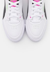 Baskets de sport blanches avec des accents noirs et des éléments en rose ; texture en cuir lisse, design à lacets, zone de pointe perforée et semelle en caoutchouc.