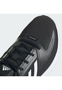 Chaussure de running Adidas noire avec tige en mesh, lacets noirs, bandes blanches sur le côté et semelle blanche, montrée en gros plan.