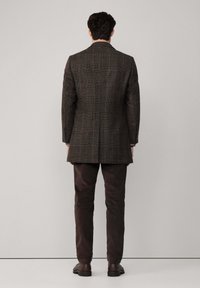 Blazer de cuadros marrones con forma ajustada, con solapa muesca y cierre de dos botones, combinado con pantalones marrones oscuros y zapatos negros.