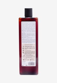 En rektangulär duschgelflaska i mörk bärnstenfärg med ett svart lock. Texturerad etikett med flerspråkig produktinformation på baksidan.
