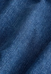Gros plan sur un tissu en denim bleu montrant une texture détaillée et un motif de tissage avec des ombres subtiles et des plis.