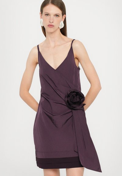Purple sleeveless dress with a deep V-neck, wrap design, and a fabric rose detail on the left side. Smooth texture with a layered hem.