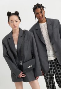 Grå oversized blazere på to personer; den ene holder en svart crossbody-veske. Den andre personen har på seg en hvit mesh-top og rutete bukser.
