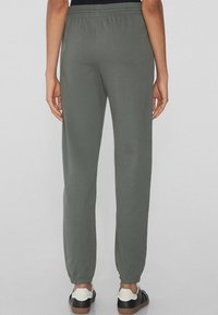 Persona vistiendo pantalones jogger grises con cintura elástica y zapatillas en blanco y negro, de pie contra un fondo claro y sencillo.