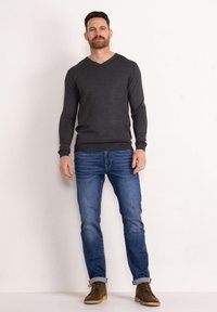 Maglione grigio scuro a V, dal design aderente, indossato con jeans azzurri. Stivali alla caviglia in suede marrone, con maniche arrotolate, texture liscia, stile casual.