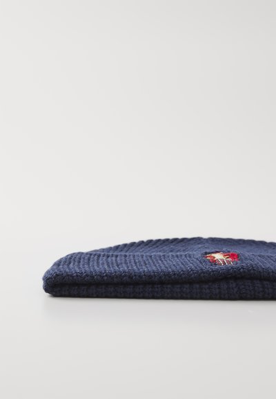 Navy-blau gestrickte Mütze mit geripptem Textur und einem kleinen gestickten Aufnäher mit einem rot-gelben Design an der Seite.