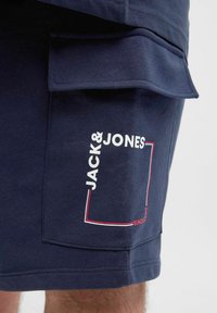 Marineblaue Cargo-Shorts mit einem auffälligen weißen Logo und roten Akzenten auf der Seiten-Tasche, gefertigt aus weichem, strapazierfähigem Material.