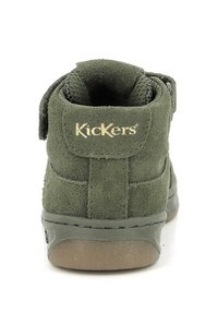 Grønn semsket ankelstøvel med borrelåsstropp, rund form, strukturert overflate og "Kickers"-logo i gull på baksiden.