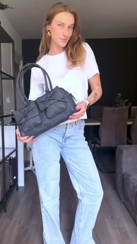 Black leather handbag with two front pockets, rounded handles, and a rectangular shape. Textured surface with subtle detailing.