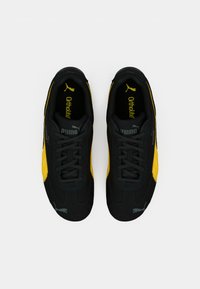 Sneaker nere e gialle con parte superiore testurizzata, dotate di lacci neri, suole Ortholite e logo Puma sul lato e sulla linguetta.