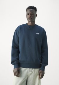 Felpa blu navy con collo a girocollo a costine e maniche con polsini, caratterizzata da un piccolo logo ricamato sul petto e una vestibilità rilassata.