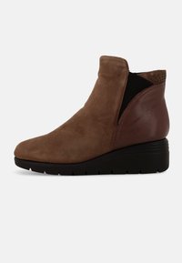 Stivale alla caviglia in suede marrone con tacco a zeppa, dotato di un pannello laterale in elastico nero e dettagli decorativi in perline sulla parte posteriore. Dettagli in pelle liscia.