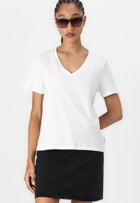 Hvit bomulls T-skjorte med v-hals og korte ermer, kombinert med et svart denimskjørt. Stoffet ser mykt ut, med en avslappet passform.