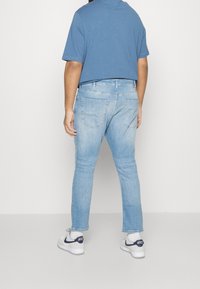 Jeans de mezclilla azul claro con un corte recto, diseño de cinco bolsillos y un sutil efecto de decolorado, combinados con una camisa azul de manga corta y zapatillas blancas.