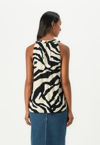 Top senza maniche in un motivo zebra crema e nero, con dettaglio a chiave sulla schiena e tessuto morbido e fluido. Abbinato a una gonna di jeans.