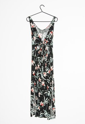 Robe maxi noire sans manches avec motif floral blanc et rouge, col en V, détail noué à l'avant, suspendue à un cintre noir sur fond blanc.