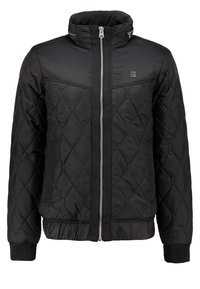 Svart vadderad jacka med hög krage, framsida med dragkedja och ribbade ärmslut. Tillverkad av ett smidigt, lätt material.