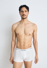 Boxer-briefs en coton blancs avec un logo Calvin Klein noir sur la ceinture, portés par un mannequin masculin torse nu sur un fond neutre.