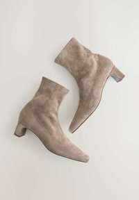Beige suede ankle boots with a pointed toe and block heel, featuring subtle stitching details along the sides. Smooth texture finish.