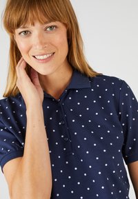 Polo shirt blu navy con pois bianchi, maniche corte e colletto, con patta dei bottoni e finitura in tessuto testurizzato.