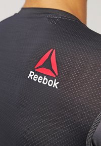 Černé sportovní tričko s texturovaným povrchem, s červeným logem Reebok a bílým nápisem na horní části zad.