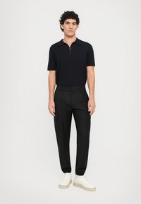 Sort kortærmet polo med lynlås i halsen, kombineret med sorte cargo-bukser og hvide sneakers, med en tætsiddende pasform og en glat stoftekstur.