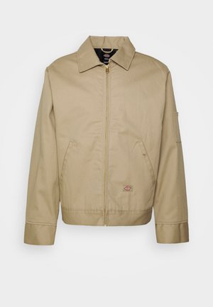 Veste en coton beige avec fermeture éclair, col classique, poches latérales et logo brodé. Présente une silhouette structurée avec un ourlet distinct.