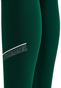 Groene leggings van rekbaar materiaal, met een witte "HUMMEL" logo aan de zijkant. Glad oppervlak, getailleerd ontwerp, ideaal voor actieve kleding.