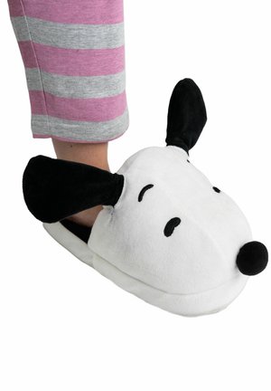 Persona che indossa pantofole a forma di cane, bianche e nere, con orecchie pendenti e un naso nero, abbinate a pantaloni a righe rosa e grigi.