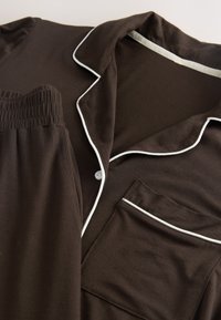 Braunes Pyjama-Set mit weißen Paspeln am Kragen, an der Tasche und an der Knopfleiste, Hose mit elastischem Bund.