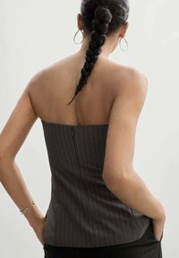 Top sans bretelles gris foncé à fines rayures, de coupe cintrée, avec une fermeture éclair au dos et une texture lisse. Le modèle porte une coiffure tressée.