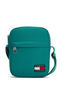 Τσάντα crossbody σε τιρκουάζ χρώμα με υφασμάτινη υφή, κλείσιμο με φερμουάρ, ρυθμιζόμενο ιμάντα και εμφανές λογότυπο με μπλε ναυτικό, λευκές και κόκκινες λεπτομέρειες.