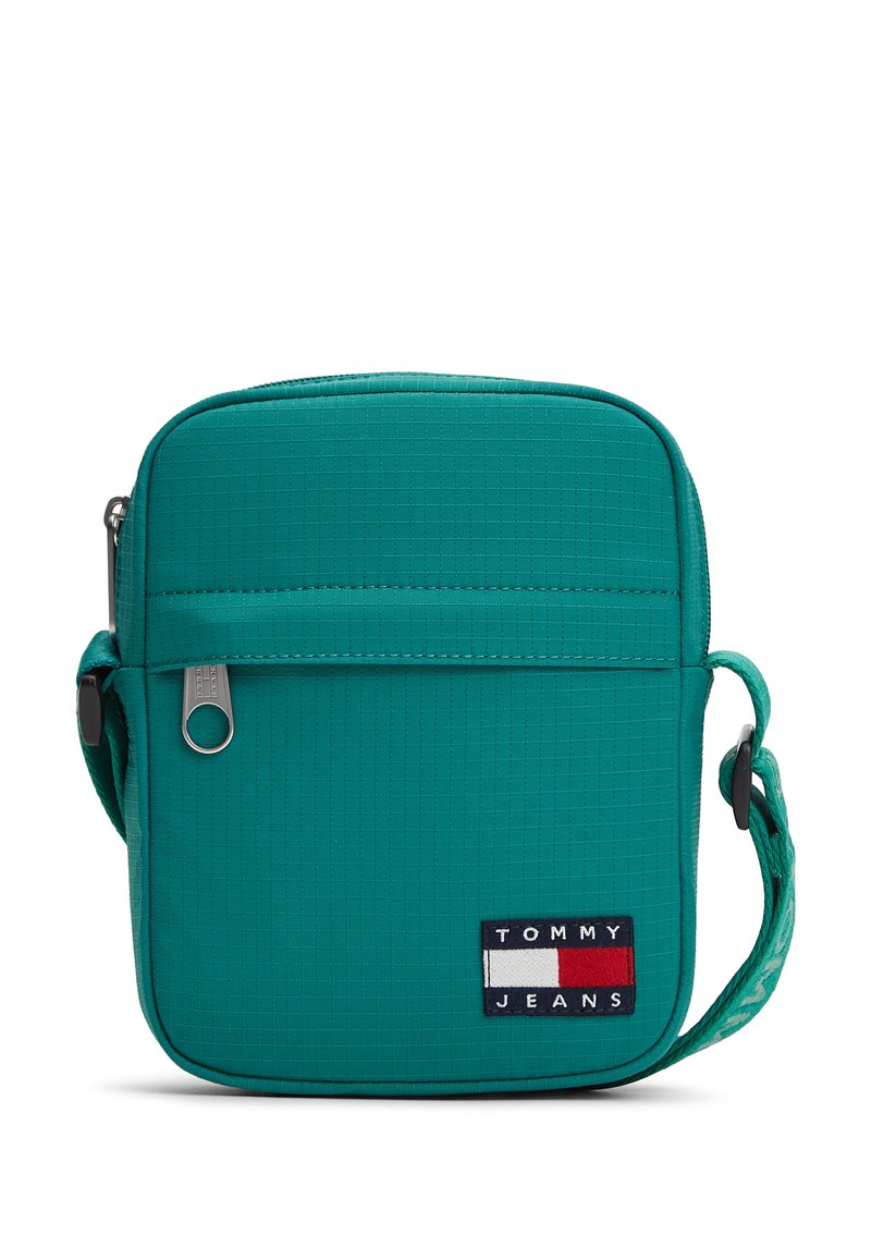 Τσάντα crossbody σε τιρκουάζ χρώμα με υφασμάτινη υφή, κλείσιμο με φερμουάρ, ρυθμιζόμενο ιμάντα και εμφανές λογότυπο με μπλε ναυτικό, λευκές και κόκκινες λεπτομέρειες.