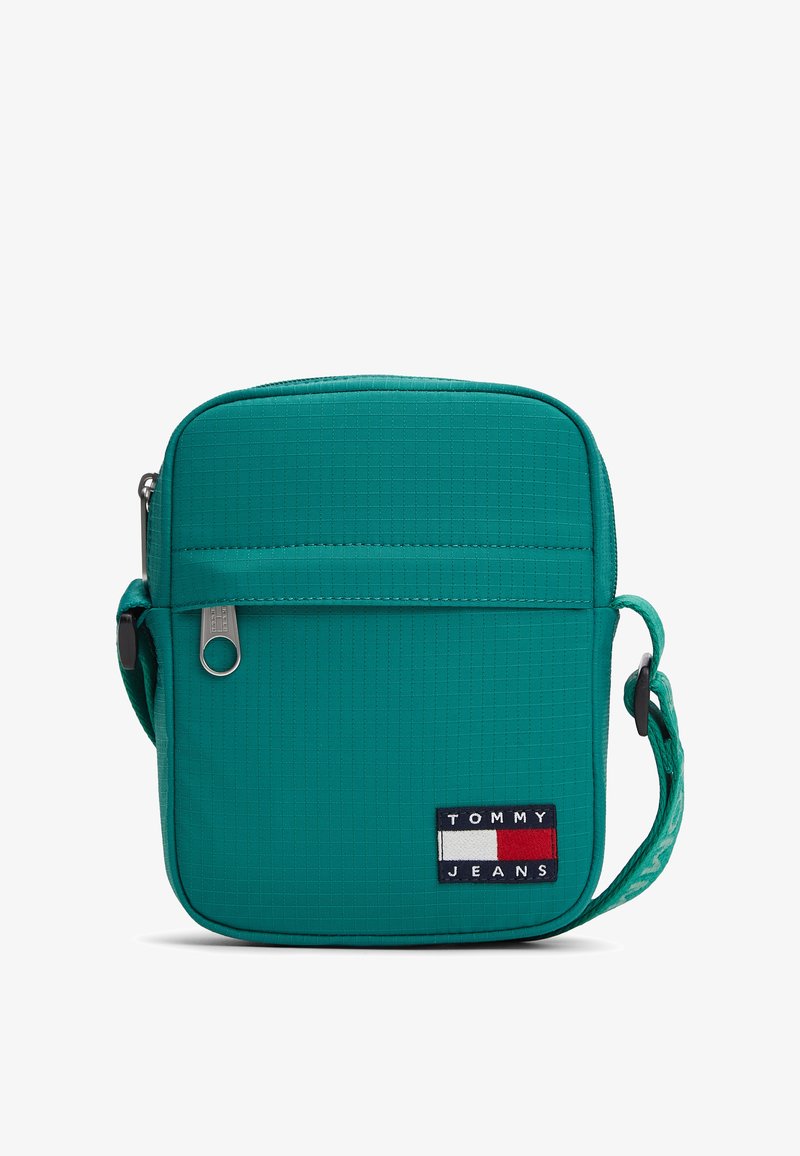 Τσάντα crossbody σε τιρκουάζ χρώμα με υφασμάτινη υφή, κλείσιμο με φερμουάρ, ρυθμιζόμενο ιμάντα και εμφανές λογότυπο με μπλε ναυτικό, λευκές και κόκκινες λεπτομέρειες.