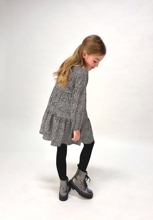 Schwarzes und weißes gemustertes Kleid mit einem gerafften Saum, kombiniert mit schwarzen Leggings und glänzenden silbernen Kampfboots. Schlichte, strukturierte Materialien.